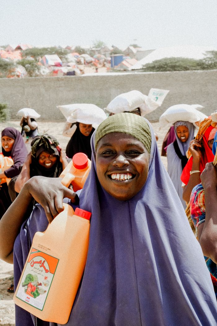 services-02 A smiling woman carries aid supplies in a community setting, Africa.