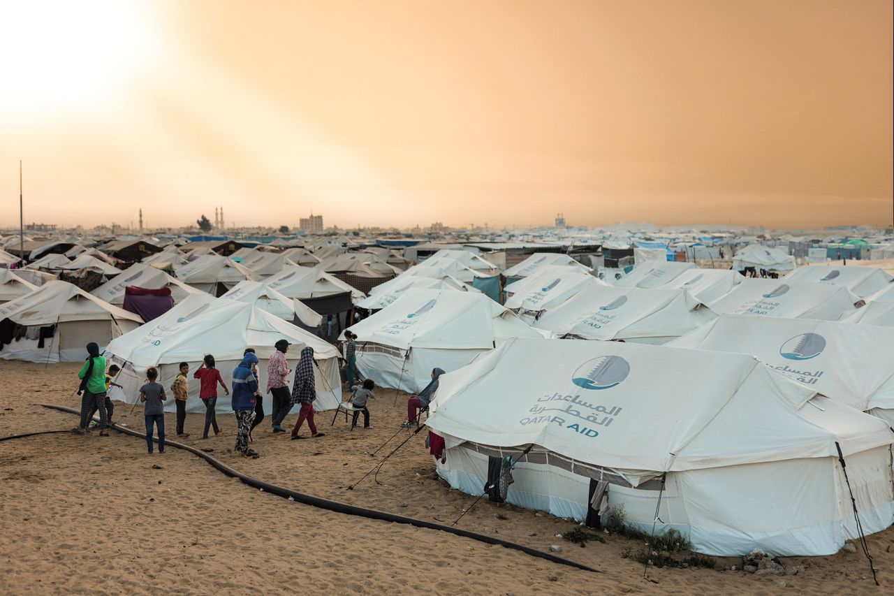 who-we-are A crowded refugee camp with aid tents at sunset, highlighting human resilience.