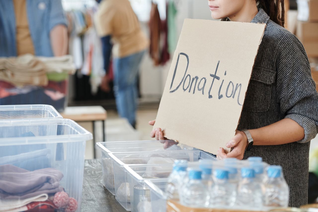 heros-img A volunteer holds a cardboard donation sign at a charity event with donation boxes ready for collection.
