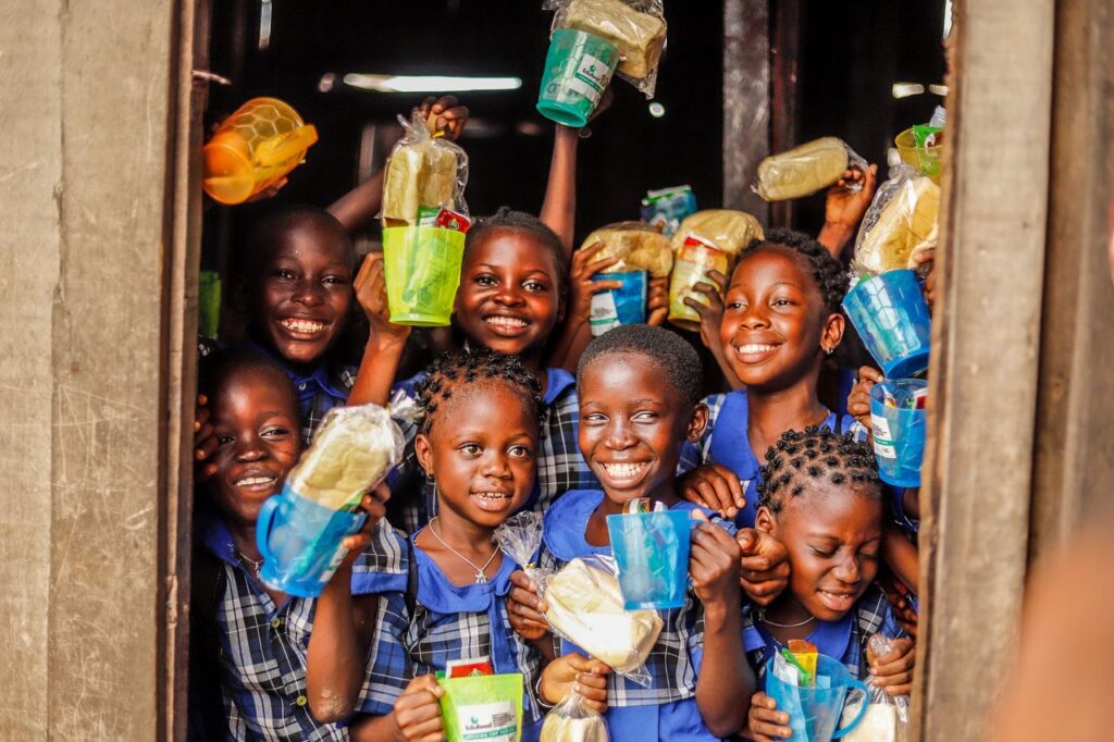 heros-img Group of happy children holding food packages and smiling outdoors.
